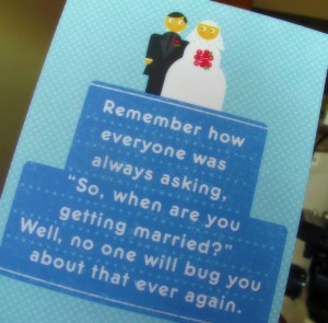 The image shows a close-up photo of the front of a wedding greeting card. The picture on the front has a cartoon of a bride and groom. below them is a message saying "Remember how everyone was always asking 'So, when are you getting married?' Well, noone will bug you about that ever again."